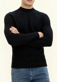 Marinblå ribbad tröja med hög krage och långa ärmar. Har en åtsittande passform och texturerad stickning. Stylingen inkluderar blå denimjeans.