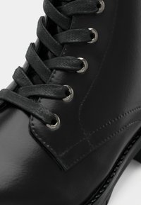 Must must pea nahk ботинк, millel on ümmargused paelad, metalliset silmused ja sile tekstuur. Otsene vaade ülemisele osale ja paelade detailidele.