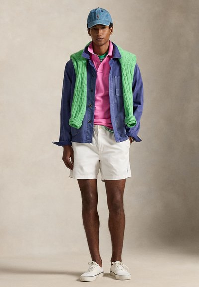 Το σύνολο περιλαμβάνει τέτοιο καπέλο από τζιν, πράσινο πουλόβερ με πλεκτό σχέδιο με κοτσίδες, ροζ πόλο, μπλε πουκάμισο, λευκά σορτς και λευκά αθλητικά παπούτσια, σε ένα casual και στιλιστικά στιβαρό layering.