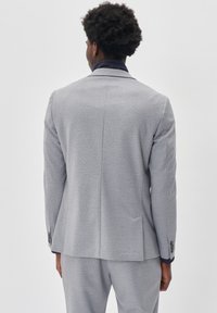 Ljust grå kavaj med strukturerad tyg, slim fit, slagknäppning och två bakventiler. Har diskret sömnad och knäppta ärmar.