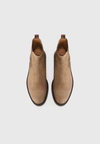 Bottes chelsea en daim marron avec des panneaux élastiques sur les côtés et des semelles en caoutchouc noir contrastantes. Dispose d'une languette pour un enfilage facile.