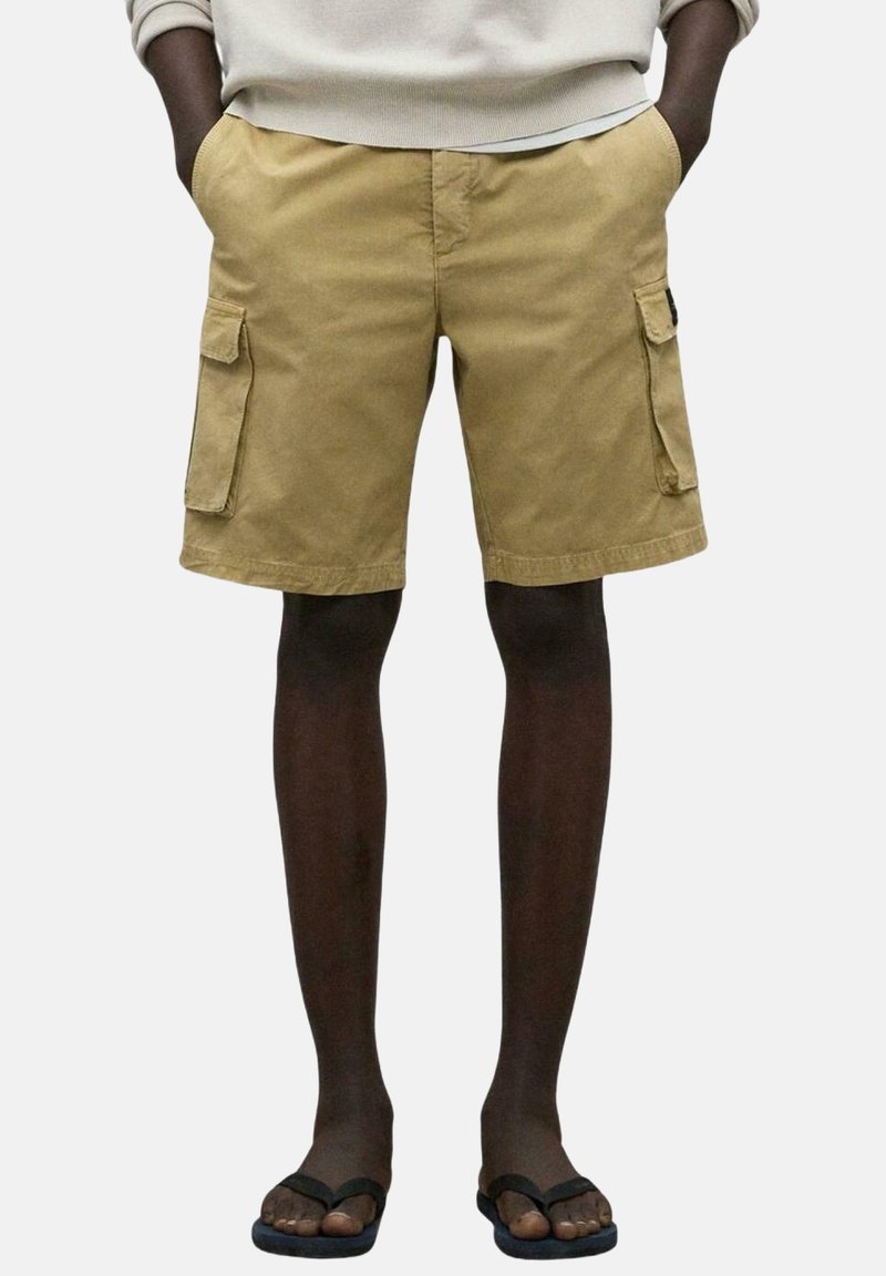 Pantalones cortos de cargo beige hechos de algodón, con bolsillos laterales, un ajuste relajado y dobladillos acabados. Combinados con chanclas negras.