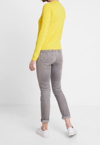 Yellow long-sleeve sweater, fitted design. Paired with light gray skinny jeans, cuffed at the ankles, and white sneakers. Plain background.