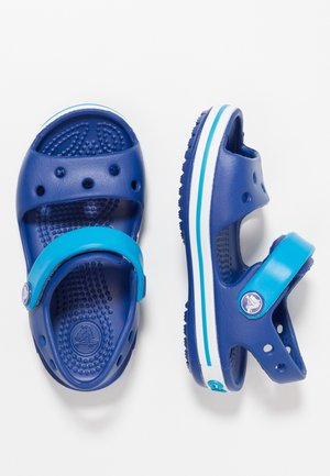 Sabots bleus pour enfants avec sangles turquoise réglables, trous de ventilation et semelles intérieures texturées, montrés vus de dessus et de côté sur fond blanc.