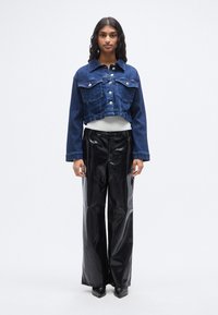 Κοντή μπλε τζιν μπουφάν με δύο μπροστινές τσέπες και κουμπιά κλεισίματος, συνδυασμένη με μαύρο ψηλόμεσο βινύλ παντελόνι και μπότες με τακούνι.