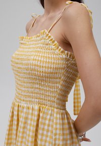Žluté a bílé kostkované letní šaty se smockovaným korzetem, tenkými ramínky a volánkovými okraji. Lehce materiál s rozšířenou sukní.