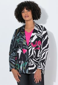 Blazer multicolore con motivi a strisce zebrate e astratti, arricchito da un'illustrazione grafica di un cane e del testo; nei colori nero, verde e rosa su un tessuto misto.