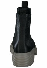 Botín negro con un upper de cuero texturizado, paneles laterales elásticos y una gruesa suela de goma gris con ranuras horizontales.