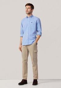 Camisa de botón azul claro con mangas remangadas, bolsillo en el pecho; combinada con pantalones cargo beige y zapatos marrón oscuro. Diseño simple, corte casual.