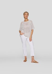 Weißes gestricktes Kurzarmoberteil mit lockerer Passform, kombiniert mit weißen cropped Hosen und beigen Rutsch-Sandalen. Sanfte Textur, lässiges Design.