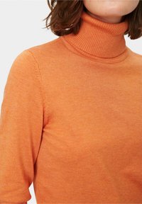 Turtlenecktröja i orange, tillverkad av ribbat stickat material, med en figurnära form och korta ärmar. Texturen verkar mjuk och slät.