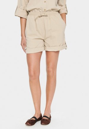 Shorts beiges avec une taille élastique et un cordon de serrage. Manches retournées et poches latérales. Tissu lisse et léger avec une coupe décontractée.