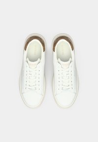 Sneakers bianchi Guess con dettagli in pelle marrone sul tallone, design con lacci e soletta con marchio, mostrati da una vista dall'alto su uno sfondo bianco.