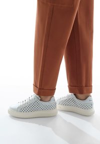 Sneakers bianchi con lati perforati, design con lacci e suola in gomma testurizzata. Abbinati a pantaloni rossi arricciati.