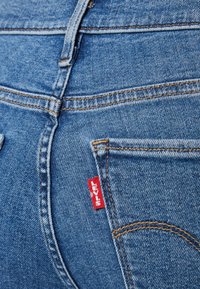 Primer plano de un bolsillo trasero de unos vaqueros de denim azul con costuras naranjas y una etiqueta roja de la marca Levi's en el lado derecho del bolsillo.