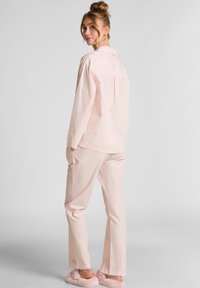 Lichtroze pyjama set met een geknoopte lange mouw shirt en rechte pijpen met subtiele verticale strepen; zachte stofafwerking en zakken.