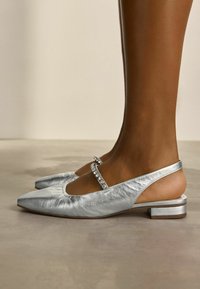 Hopeiset, metalliset slingback-ballerinat, joissa on terävä kärki, ja joissa on strassin yksityiskohta hihnassa sekä matala lohkopohja.