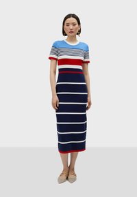 Stickad klänning med blå, röda och vita horisontella ränder. Korta ärmar, rund halsringning och midi-längd. Mjuk textur med en figurnära siluett.