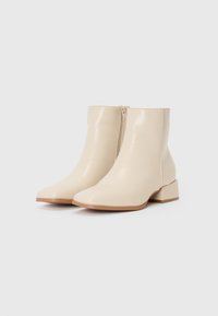Bottines beiges avec une finition brillante, bout pointu et un petit talon carré. Dispose d'une fermeture éclair sur le côté pour un enfilage facile.