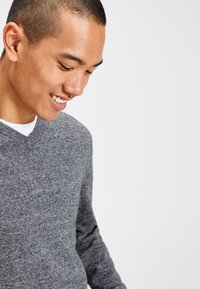 Grauer Strickpullover mit V-Ausschnitt, langen Ärmeln und weicher Textur. Der Stoff wirkt leicht und lässig.