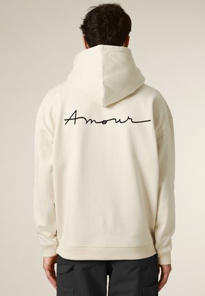 Cream hoodie with a large, black "Amour" embroidery on the back. Features a ribbed hem and cuffs, and a drawstring hood for a relaxed fit.