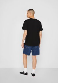 Svart T-skjorte med korte ermer, denimshorts og svarte sneakers med hvite såler. Enkelt, avslappet design. Hvit bakgrunn gir kontrast.