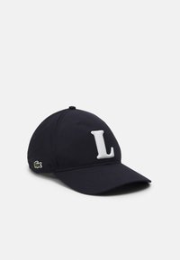Granatowa czapka baseballowa z białym haftowanym "L" z przodu oraz małym zielonym logo krokodyla z boku. Materiał bawełniany, zakrzywiony daszek.