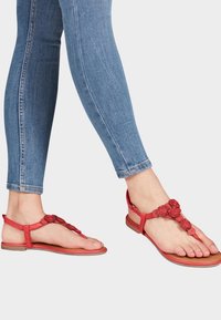 Chanclas rojas con acentos de flores; hechas de material sintético. Suela plana, diseño de punta abierta, combinadas con jeans skinny azules.