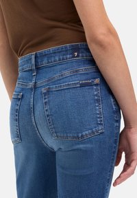 Niebieskie dżinsy z denimu z średnim stanem, wyposażone w tylne kieszenie, jasne przeszycia i gładką fakturę.