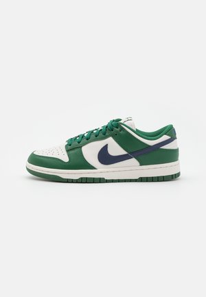 Baskets basses en cuir vert et blanc, virgule Nike bleu marine, lacets verts et semelle blanche avec bande de roulement verte.