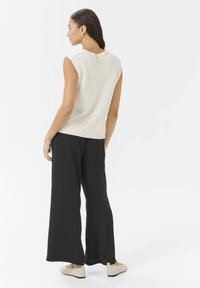 Beige knitted vest with a round neckline, paired with loose black wide-leg pants and beige flats, viewed from the back.