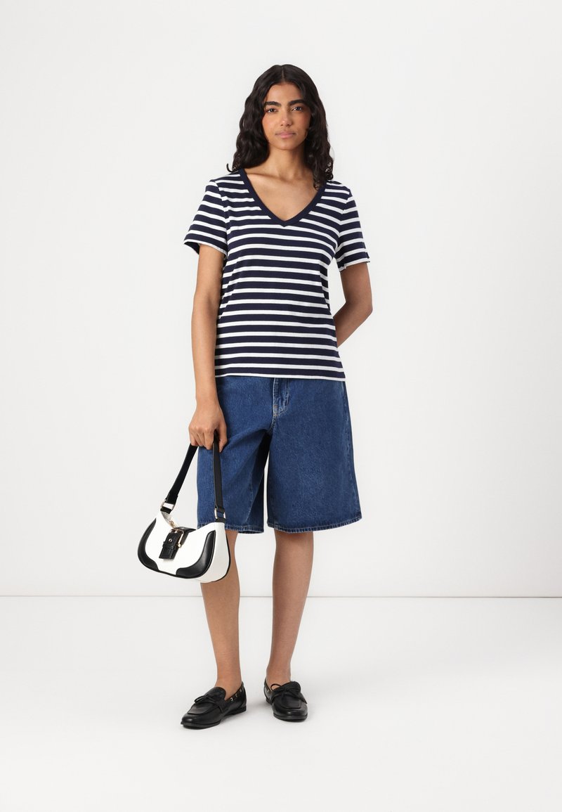 Marynarska koszulka w paski w kolorze granatowym i białym, dżinsowe bermudy, czarne mokasyny oraz mała czarna torebka w biało-czarnym kolorze.