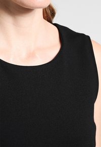 Svart ärmlös topp med rundad halsringning. Tyget verkar slätt och elastiskt, vilket ger en figursydd siluett. Inga påtagliga mönster eller detaljer.