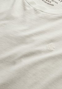 Hvid bomulds T-shirt med rund hals, der har et lille broderet logo i det nederste hjørne. Blød tekstur og glat overflade.