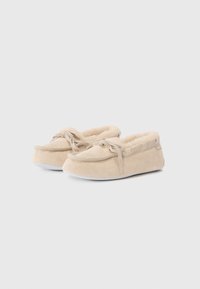 Chaussures slip-on en suède beige avec doublure intérieure douce, bout arrondi et nœud décoratif à l'avant. Semelle en caoutchouc pour une meilleure adhérence.