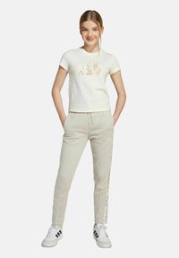 Witte katoenen t-shirt met bloemenprint, gecombineerd met lichtbeige joggingbroek met zijkanten, gedragen met witte sneakers.