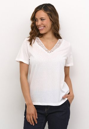 White short-sleeve t-shirt featuring a decorative lace V-neckline, soft fabric, and a relaxed fit. Paired with dark blue jeans.