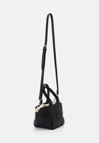 Svart vävd handväska med en stram form, som har en avtagbar svart rem och en texturerad vit inredning med en rynkad kant.