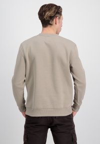 Světle béžová mikina s kulatým výstřihem, dlouhými rukávy a žebrovaným lemem. Vyrobená z měkkého materiálu, obsahuje minimalistický design.