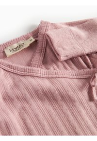 Gros plan sur un vêtement rose doux avec une texture côtelée et un cordon de serrage. Une étiquette indique "Marmar Copenhagen", taille 56, avec une manche repliée à proximité.