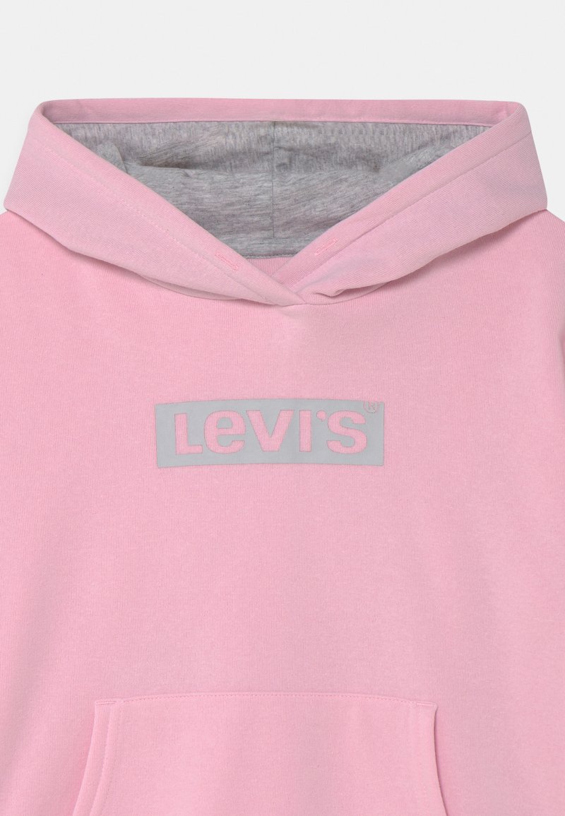 Sweat à capuche rose avec une doublure en polaire grise, arborant un grand logo Levi's gris à l'avant et une poche frontale. Texture de tissu douce.