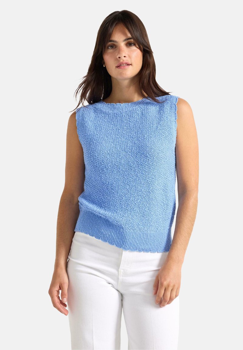 Lichtblauwe mouwloze pullovertrui met een gestructureerde brei, geribbelde zoom en geschulpte halslijn, gecombineerd met een witte broek.