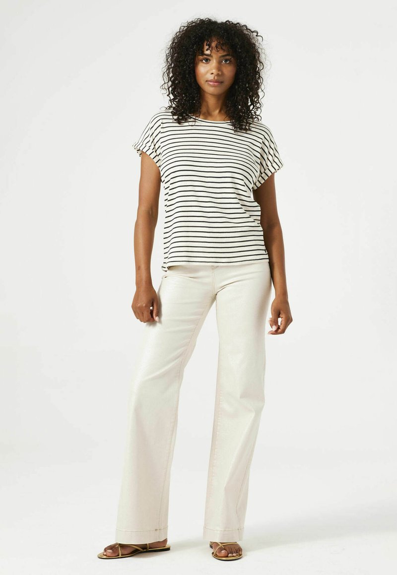 Gestreepte top met korte mouwen in crème en zwart, gecombineerd met wijde crème broek. Sleehakken maken de outfit af.
