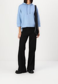 Sudadera con capucha de color azul claro y mangas anchas, combinada con pantalones negros acampanados y zapatos negros gruesos, llevada con un bolso negro.