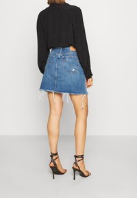 Jeanskjol med fransad nederkant, blå färg, hög midja. Svart långärmad topp och svarta klackar med remmar fulländar outfiten.