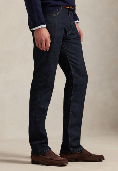 Temno modre kavbojke iz jeansa z ravnim krojem hlačnic, s kontrastnimi šivi, zadnjimi žepi in nošene s rjavimi antilop natikači.