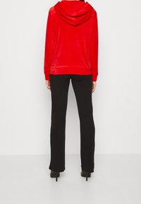 Sudadera de terciopelo rojo con capucha, de corte holgado y mangas largas, combinada con pantalones negros ajustados y zapatos de tacón alto.