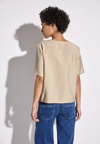 Beige krátký rukáv top s jemnou, texturovanou úpravou, v kombinaci s modrými džínami s kapsami na zadní straně a uvolněným střihem.