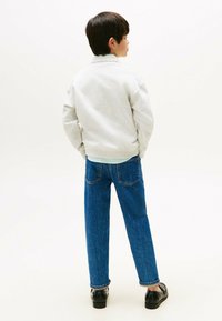Felpa grigia con polsini e orlo a costine, abbinata a jeans denim blu e scarpe nere. I jeans hanno una vestibilità rilassata e cuciture visibili.