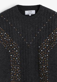 Suéter de canalé gris oscuro con acentos decorativos de tachuelas y estrellas doradas y plateadas a lo largo del frente en un patrón diagonal.